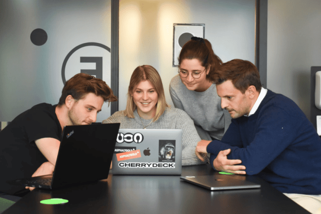 Four people sitting around a table looking at a laptop.