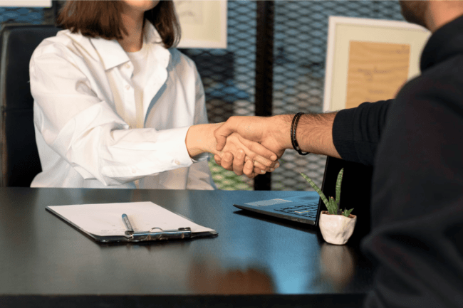 A person shaking hands with another person at a desk.