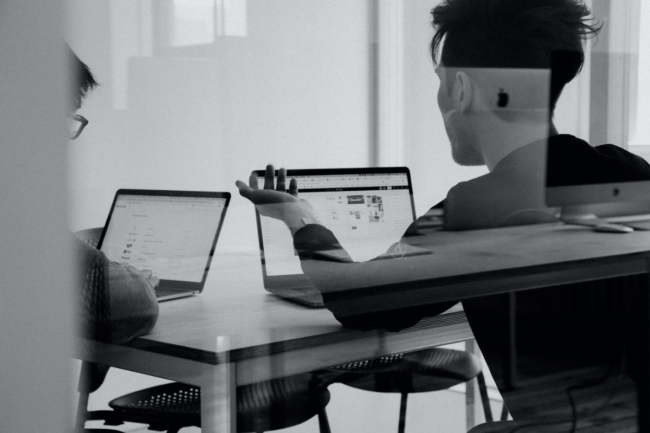 A black and white photo of two people working on laptops.